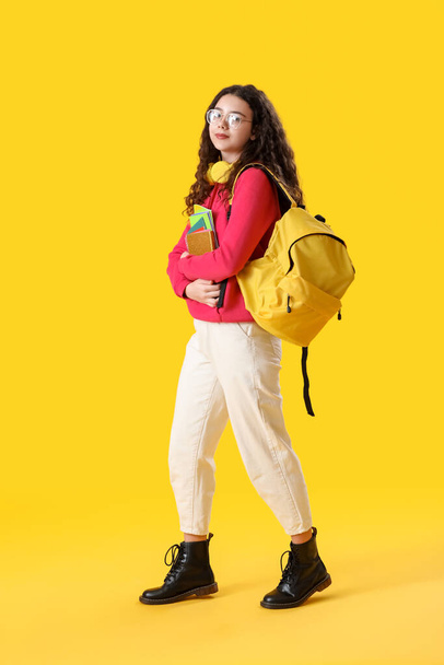 Női hallgató fejhallgató, notebook és hátizsák sárga háttér - Fotó, kép