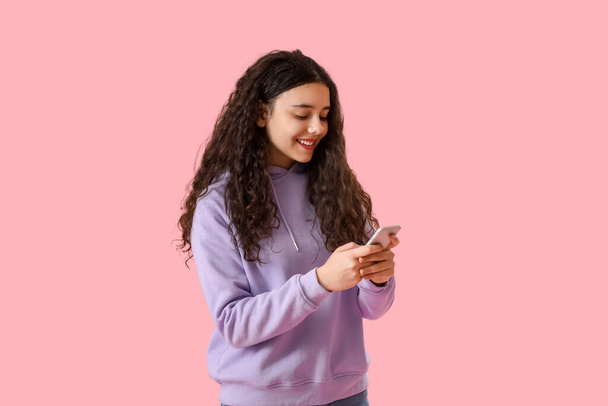 Nastolatka w kapturze za pomocą telefonu komórkowego na różowym tle - Zdjęcie, obraz