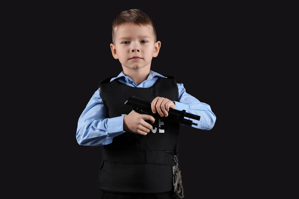 Cute little police officer with gun on black background - Фото, изображение