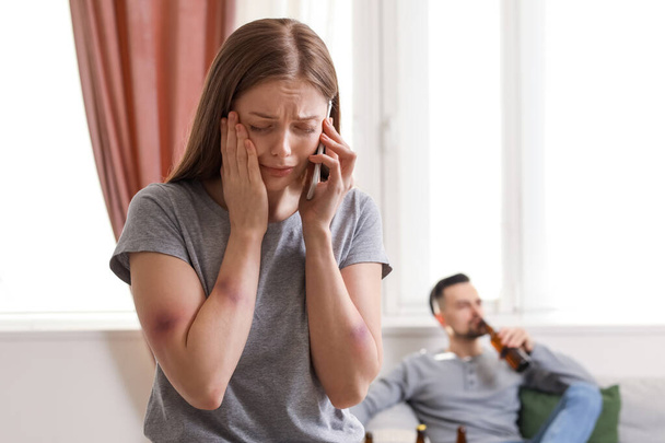 Ушибленная молодая женщина разговаривает по мобильному телефону дома. Концепция домашнего насилия - Фото, изображение