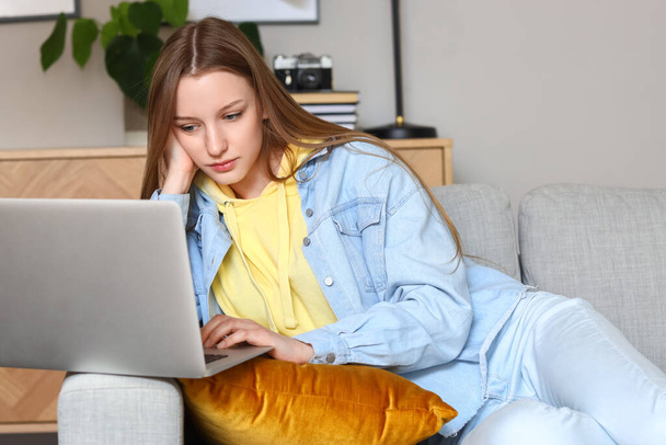 Nachdenkliches Teenager-Mädchen benutzt Laptop auf Sofa zu Hause - Foto, Bild