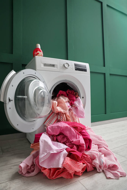 Çamaşır odasında yeşil duvarın yanında kirli çamaşırları olan çamaşır makinesi. - Fotoğraf, Görsel