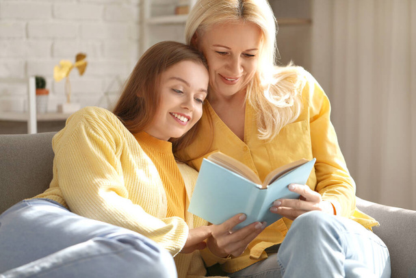 Young woman with her mother reading book at home - Foto, afbeelding