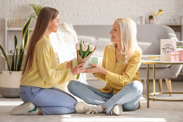 Young woman greeting her mother with tulips and gift at home - Foto, Imagen