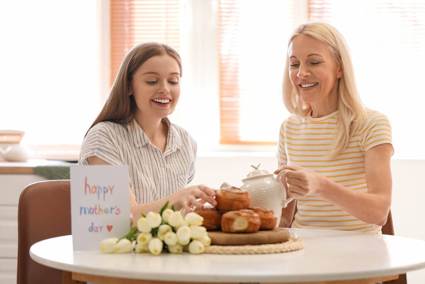 Mature woman with her daughter drinking tea in kitchen. Mother's Day celebration - Foto, imagen
