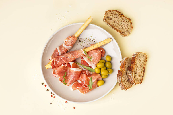 Plate with slices of tasty jamon and Italian Grissini on yellow background - Photo, Image