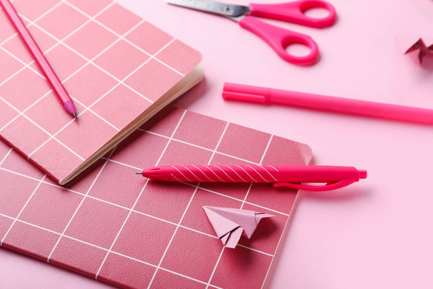 Samenstelling met notitieboekjes, briefpapier benodigdheden en papier vliegtuig op roze achtergrond - Foto, afbeelding