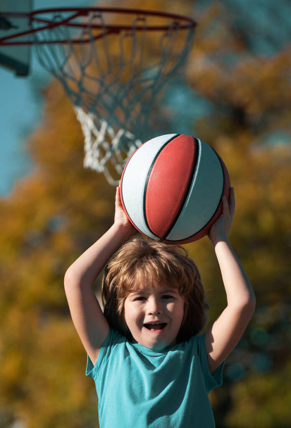 Cute smiling boy plays basketball. Active kids enjoying outdoor game with basket ball - Zdjęcie, obraz