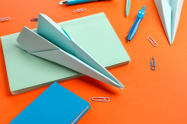 Composition with stationery supplies and paper planes on orange background - Fotó, kép