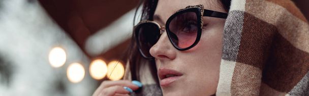 Nahaufnahme einer attraktiven, stylischen jungen brünetten Frau mit Sonnenbrille, bedeckt mit buntem Schal. - Foto, Bild