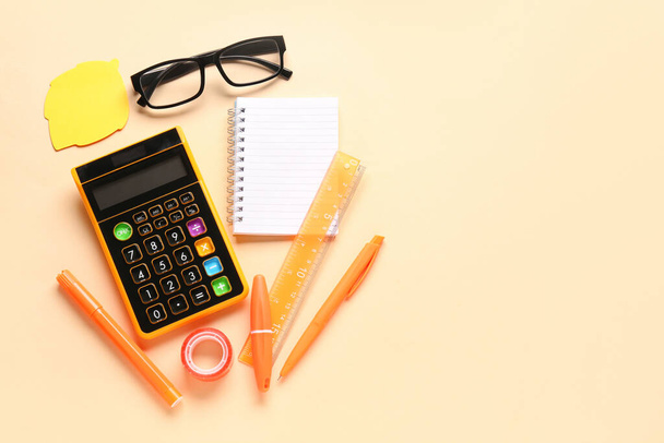 Calculadora, gafas y artículos de papelería sobre fondo beige - Foto, Imagen