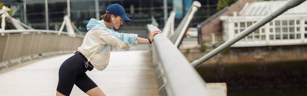Sportive woman doing stretching exercise on footbridge in the city. Healthy lifestyle - Photo, Image