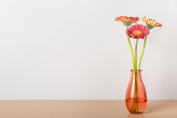 Vase mit Gerbera-Blumen auf dem Tisch in der Nähe der Lichtwand - Foto, Bild