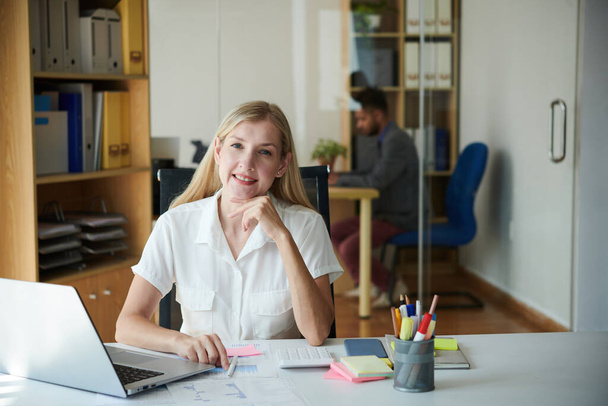 Portrait of smiling entrepreneur working with documents at office desk - Photo, Image