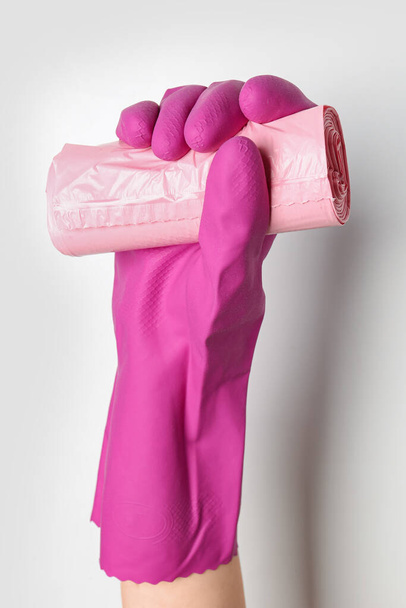 Hand in rubber glove with roll of garbage bags on white background - Foto, imagen