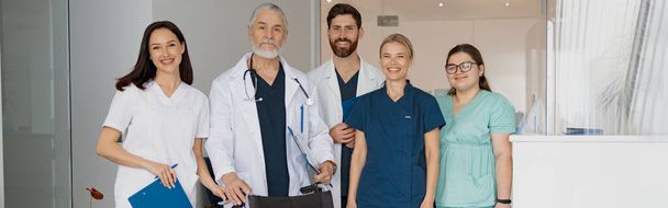 Група професійних лікарів в уніформі, що стоїть в клінічному залі з медичним інвалідним візком в клініці
 - Фото, зображення