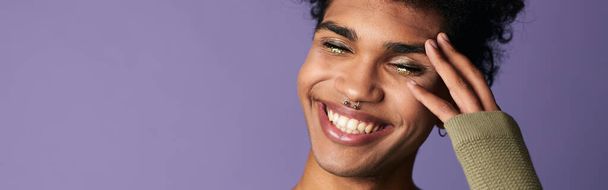 Zbliżenie uśmiechnięty Afrykański amerykański mężczyzna z afro fryzurą. Portret przystojnego transseksualisty. Szczęśliwy casual ubrany trans model płci na fioletowym tle. Moda - Zdjęcie, obraz