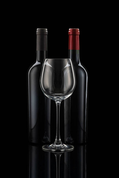 Two wine bottles next to each other, a wine glass in front of a black background - 写真・画像