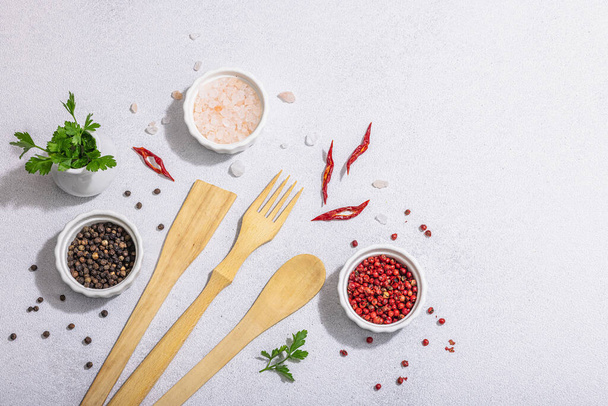 Culinary background with wooden kitchen utensil, spices and herbs. Set for preparation healthy food, flat lay. Hard light, dark shadow, light stone concrete background, top view - 写真・画像