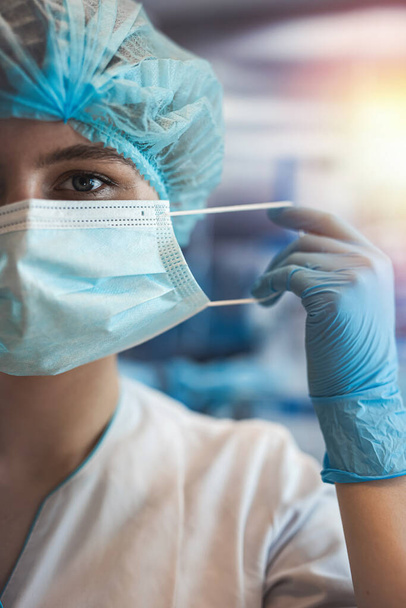 Portrait of young female woman surgeon wearing protective cloth surgical mask in operation room. Healthrace worker - 写真・画像