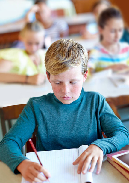Er ist ein fleißiger Schüler. Ein kleiner Junge schreibt im Unterricht in sein Notizbuch - Foto, Bild