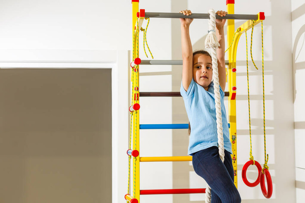Beautiful athletic girl plays sports on Wall bars in the childrens room. - Foto, Bild