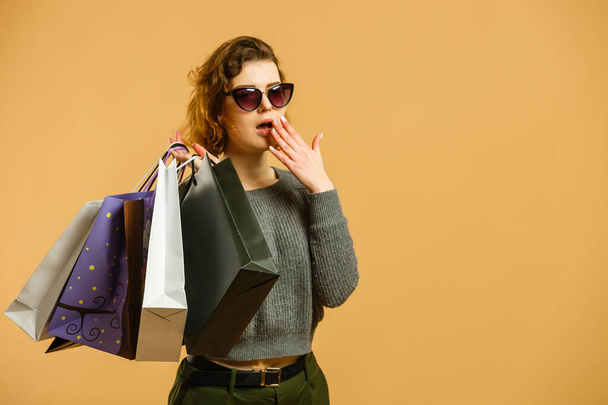 Porträt eines aufgeregten schönen Mädchens mit Sonnenbrille, das Einkaufstüten isoliert vor beigem Hintergrund hält. - Foto, Bild