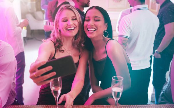 Was wäre eine Party ohne all die Selfies. zwei junge Frauen machen gemeinsam ein Selfie in einem Nachtclub - Foto, Bild