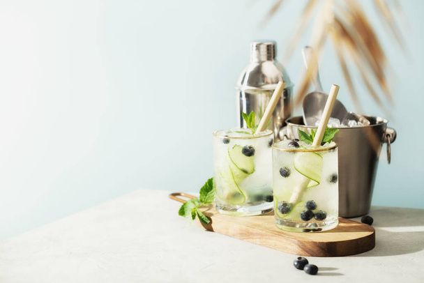 Trendy summer drinks with cucumber, mint and blueberry and Bar accessories on blue sky background - Photo, Image