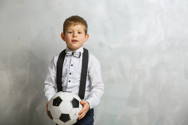 kleine jongen met een voetbal op een grijze achtergrond - Foto, afbeelding