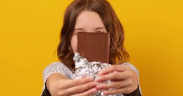 ładna nastolatka dziewczyna z czekolada bar izolowane na studio żółty tło, korzystających z deser, przestrzeń kopia - Materiał filmowy, wideo