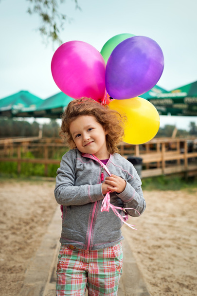 Little girl with balloons on the sandy bank of the river or lake. - Zdjęcie, obraz