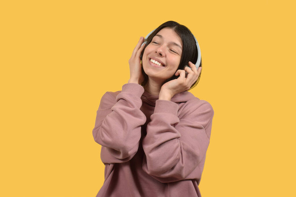 Egy rózsaszín pulóvert és rózsaszín pulóvert viselő nő mosolyog és zenét hallgat a fejhallgatóján.. - Fotó, kép