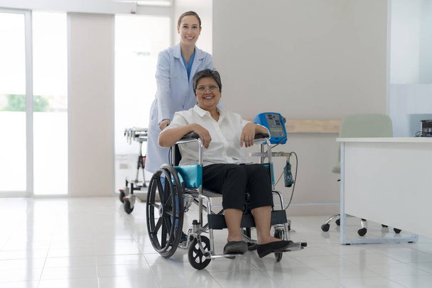 Doctor helping senior patient push wheelchair in hospital interior. - Foto, imagen