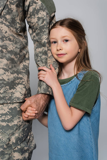 cute preteen girl hugging hand of father in military uniform isolated on grey  - Φωτογραφία, εικόνα