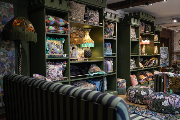 LONDON - April 17 2023 Liberty's, Luxury department store English interior in dark colors. Lamps with lampshades, cushions on cabinet shelves, sofa, bedspreads for sale in the interior department - 写真・画像