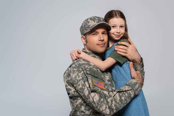 Ευτυχισμένο κορίτσι αγκαλιάζει τον πατέρα με στρατιωτική στολή κατά τη διάρκεια της ημέρας μνήμης απομονωμένο σε γκρι  - Φωτογραφία, εικόνα
