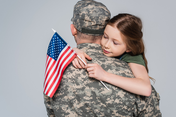 katona katonai egyenruhában ölelés lánya amerikai zászló elszigetelt szürke  - Fotó, kép