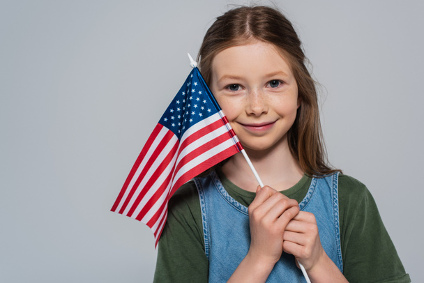 Весела і патріотична дівчина тримає прапор Сполучених Штатів Америки в день пам'яті ізольований на сірому  - Фото, зображення