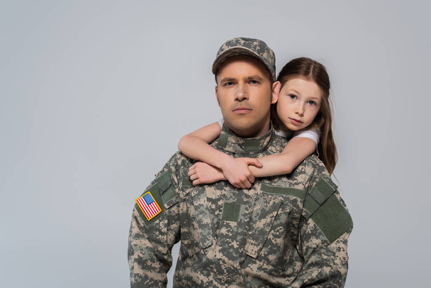 preteen fille étreignant courageux père en uniforme de l'armée pendant la journée commémorative isolé sur gris  - Photo, image