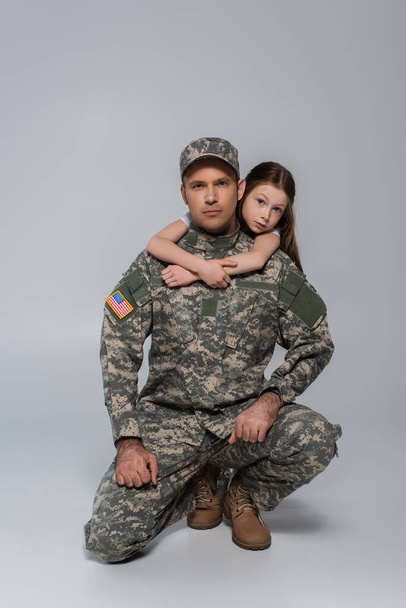 criança pré-adolescente abraçando pai corajoso em uniforme do exército durante o dia comemorativo em cinza  - Foto, Imagem