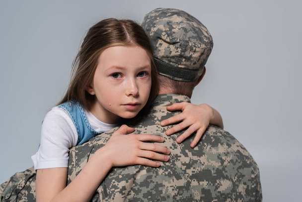 menina patriótica abraçando o pai em uniforme do exército e chorando durante o dia comemorativo isolado no cinza - Foto, Imagem