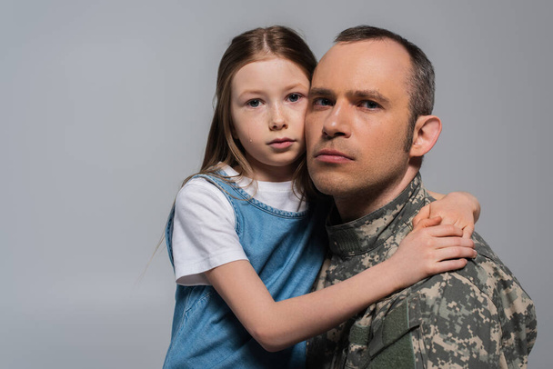 bambino patriottico che abbraccia l'uomo militare in uniforme e piange durante il giorno commemorativo isolato su grigio - Foto, immagini