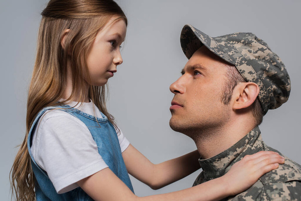 triste fille regardant militaire en uniforme militaire pleurer pendant la journée commémorative isolé sur gris  - Photo, image