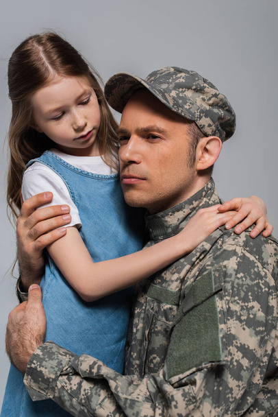 triste fille étreignant militaire en uniforme militaire pleurer pendant la journée commémorative isolé sur gris  - Photo, image