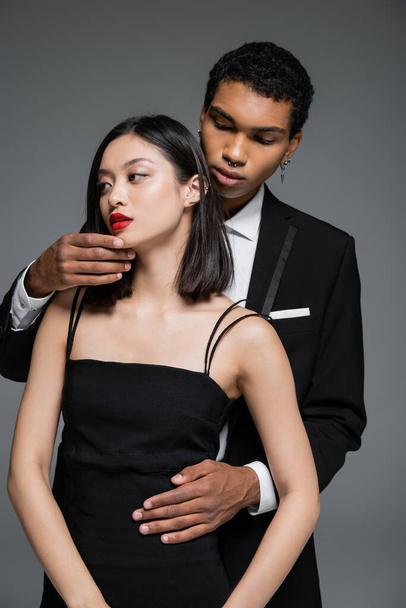 young african american man touching chin of elegant asian woman with red lips isolated on grey - Φωτογραφία, εικόνα