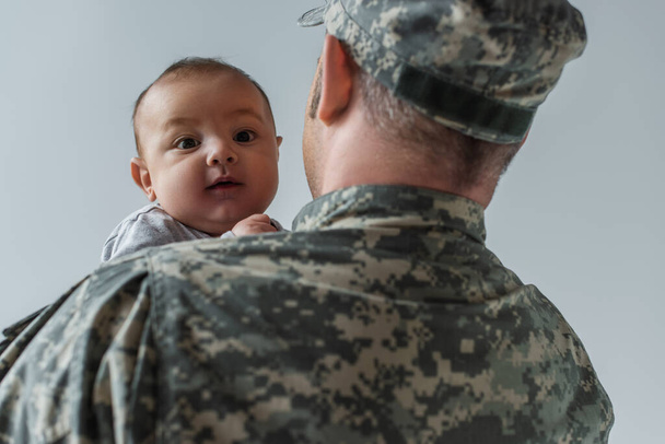 Gri yolda askeri üniformalı asker kollarındaki yeni doğan çocuk.  - Fotoğraf, Görsel