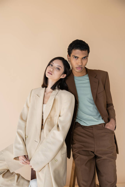 interracial couple in fashionable blazers looking at camera isolated on beige - Photo, Image