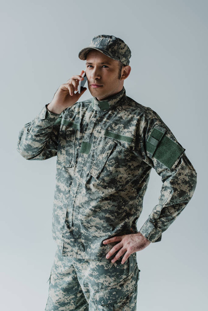 serviceman in cap and army uniform talking on smartphone isolated on grey  - Zdjęcie, obraz