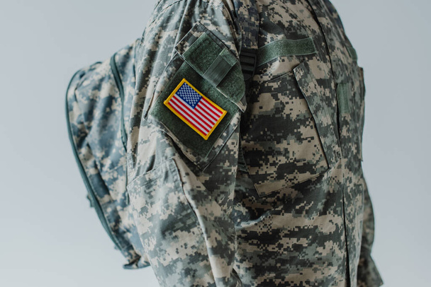 Ausgeschnittene Ansicht eines amerikanischen Soldaten in Armeeuniform, der mit Rucksack isoliert auf grau steht  - Foto, Bild